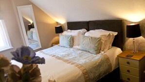 A neatly made bed with a headboard, two bedside tables with lamps, and a mirror on the wall. - The Sherwood (Skegness)