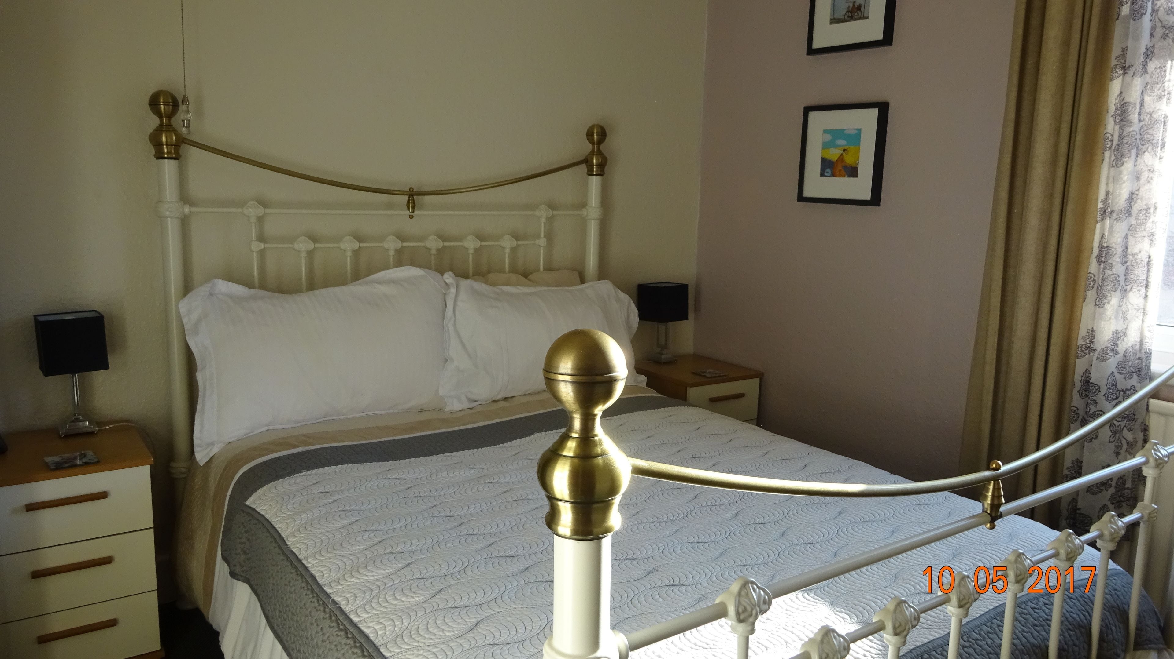 A neatly made bed with a white headboard, two bedside tables with lamps, and a window with curtains.