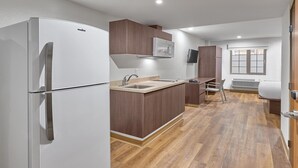A compact kitchen with a white refrigerator, wooden cabinets, a built-in microwave, and a window with a view. - Extended Suites Ciudad Juarez Consulado (Ciudad Juárez)