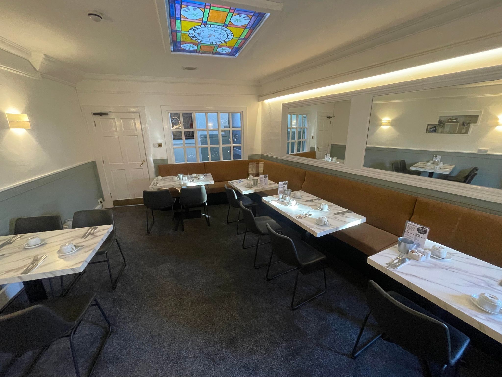 Een restaurant met zitjes, tafels, een glas-in-loodraam en een spiegel aan de muur.