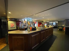Zona de bar con mostrador, diversas botellas y un cartel que indica una oferta especial.