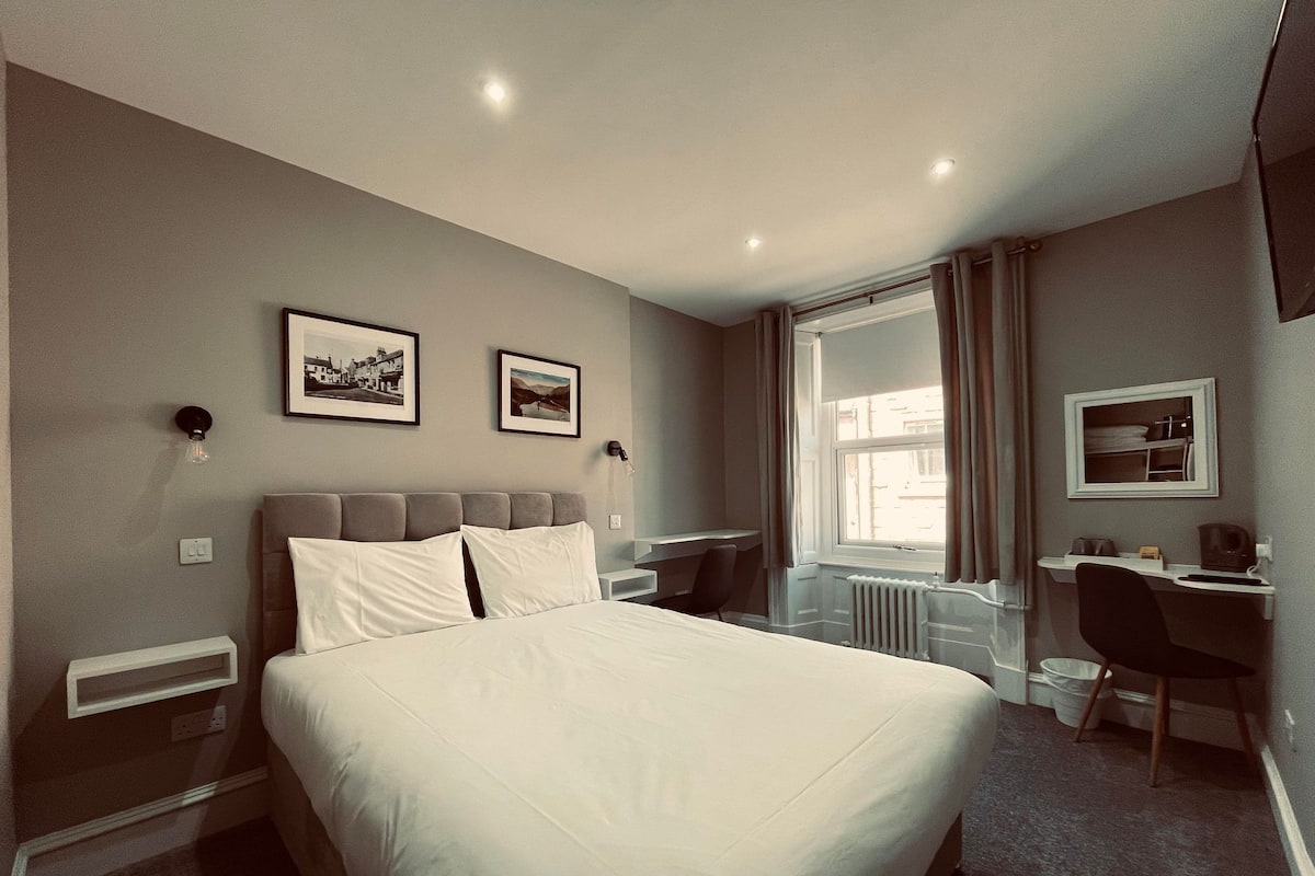 Ein modernes Hotelzimmer mit einem großen Bett, einem Schreibtisch und zwei gerahmten Bildern an der Wand.