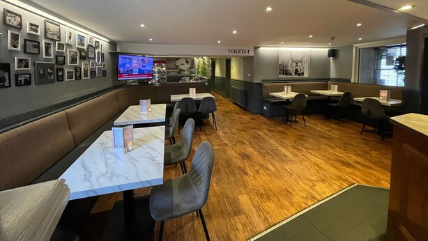 Een modern restaurant met marmeren tafels en comfortabele zitjes, een televisie waarop een nieuwsuitzending draait, en een bord dat de locatie van de toiletten aangeeft.