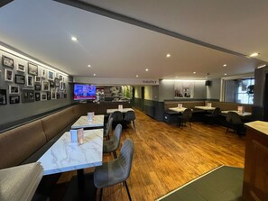 Een modern restaurant met marmeren tafels en comfortabele zitjes, een televisie waarop een nieuwsuitzending draait, en een bord dat de locatie van de toiletten aangeeft.