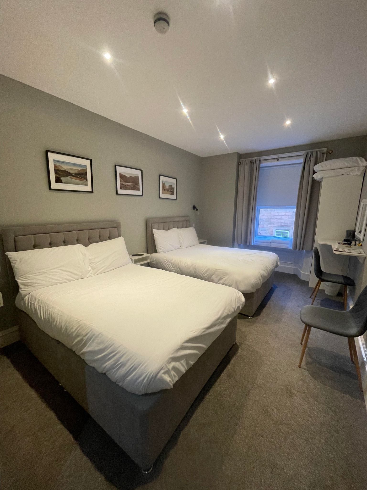 Une chambre d’hôtel avec deux lits, un bureau, une chaise et une fenêtre avec des rideaux.