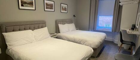 Une chambre d’hôtel avec deux lits, un bureau, une chaise et une fenêtre avec des rideaux.