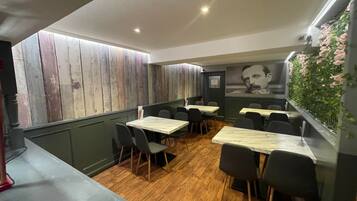 A restaurant interior with wooden panel walls, tables with chairs, and a green wall with flowers.
