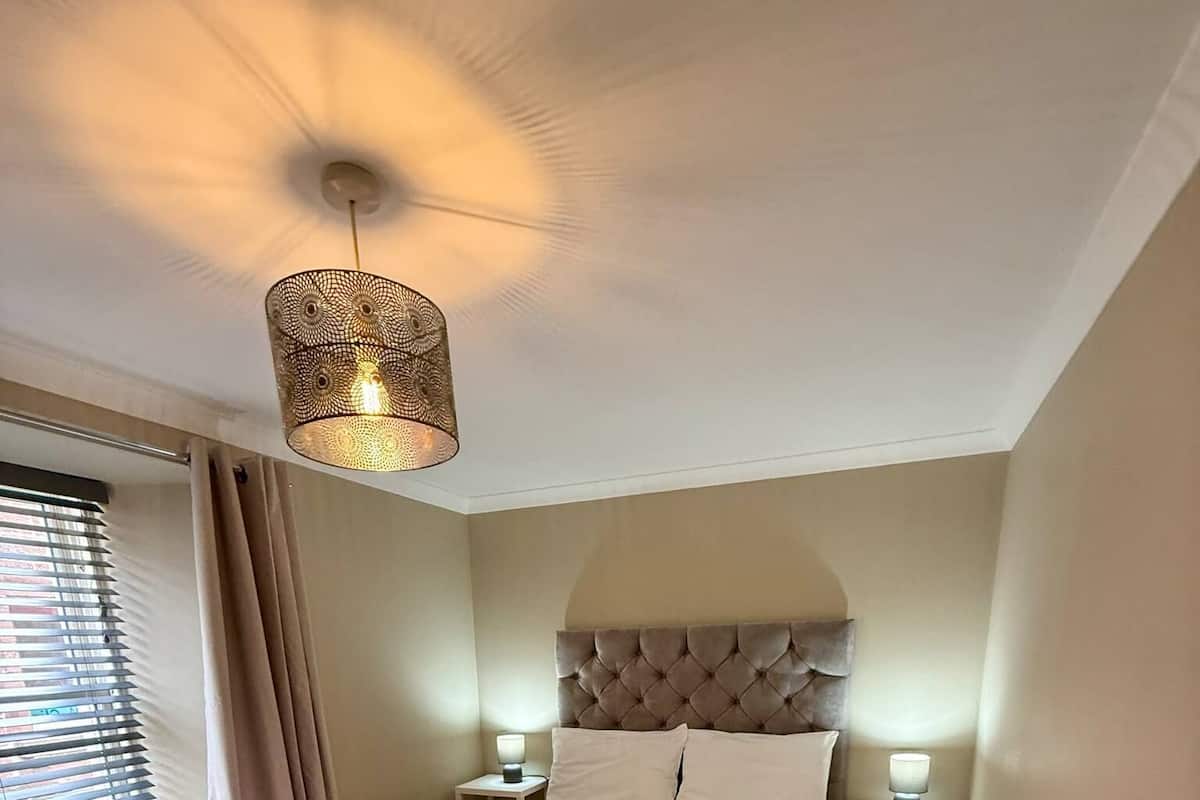 Ein Schlafzimmer mit einem großen Bett, zwei Nachttischen, einer Deckenleuchte und einem Fenster mit Vorhängen.