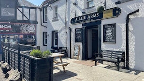 Een traditionele pub genaamd Airlie Arms, met een bord, terras en een stenen muur.