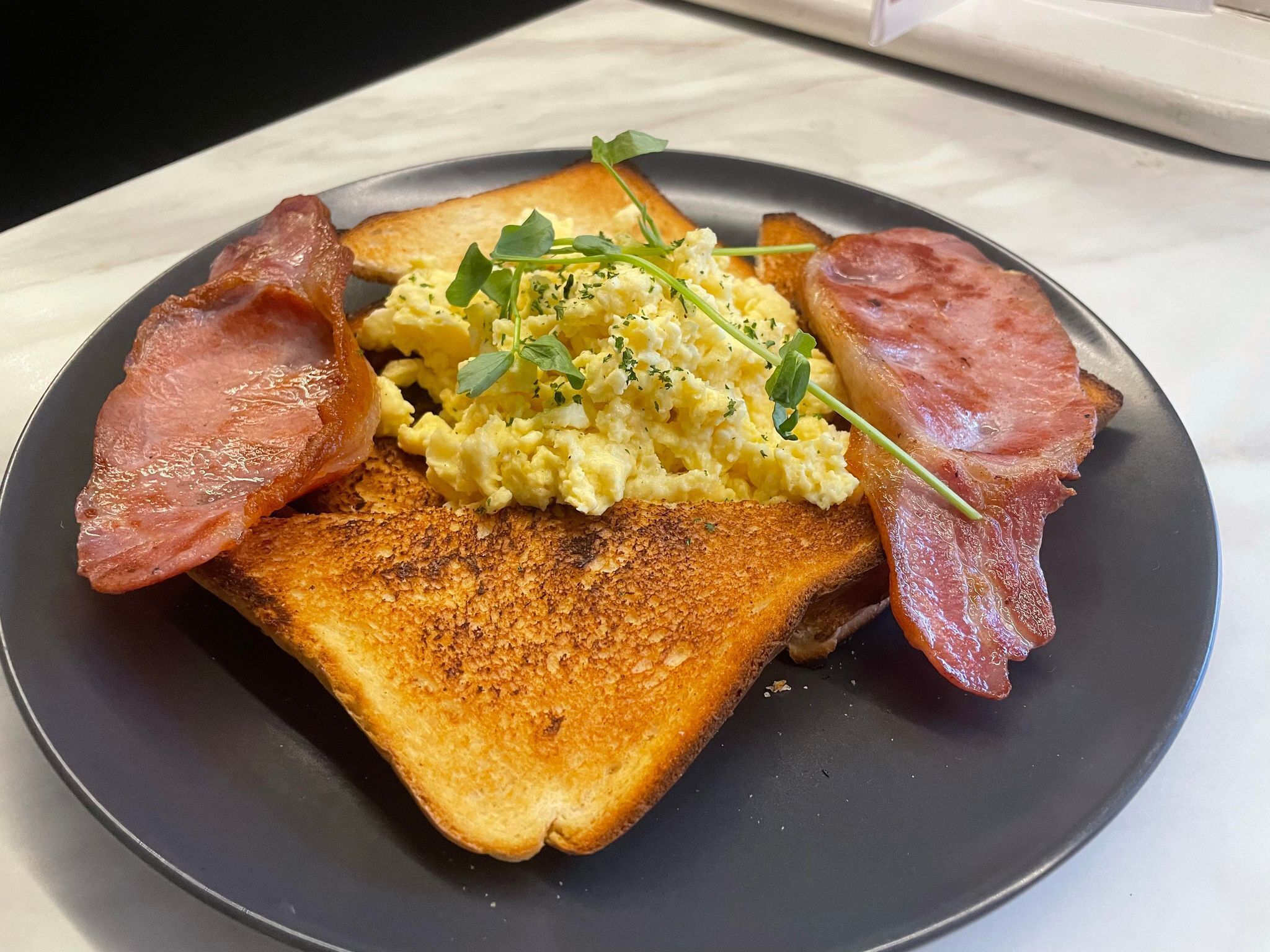 Une assiette avec des œufs brouillés, des toasts et des tranches de jambon.