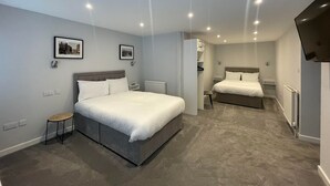 Een moderne hotelkamer met twee bedden, een klein krukje en een televisie.