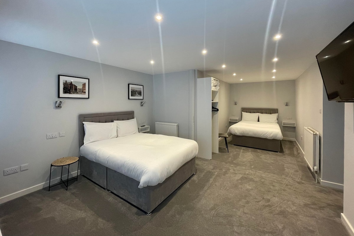 Ein modernes Hotelzimmer mit zwei Betten, einem kleinen Hocker und einem Fernseher.