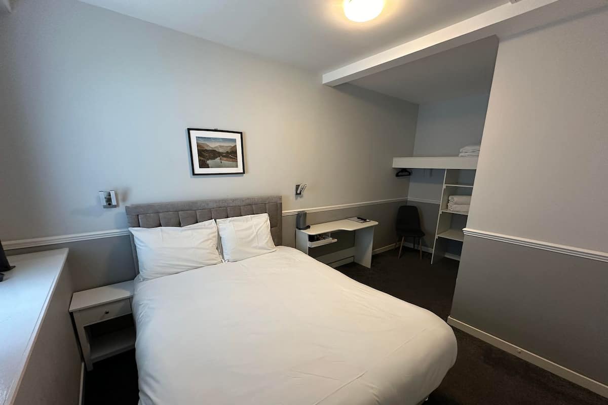 Ein Hotelzimmer mit Bett, Schreibtisch, Stuhl, Kleiderschrank und einem gerahmten Bild an der Wand.