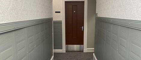 A hallway with a carpeted floor, white walls, and a door marked with the number 5.