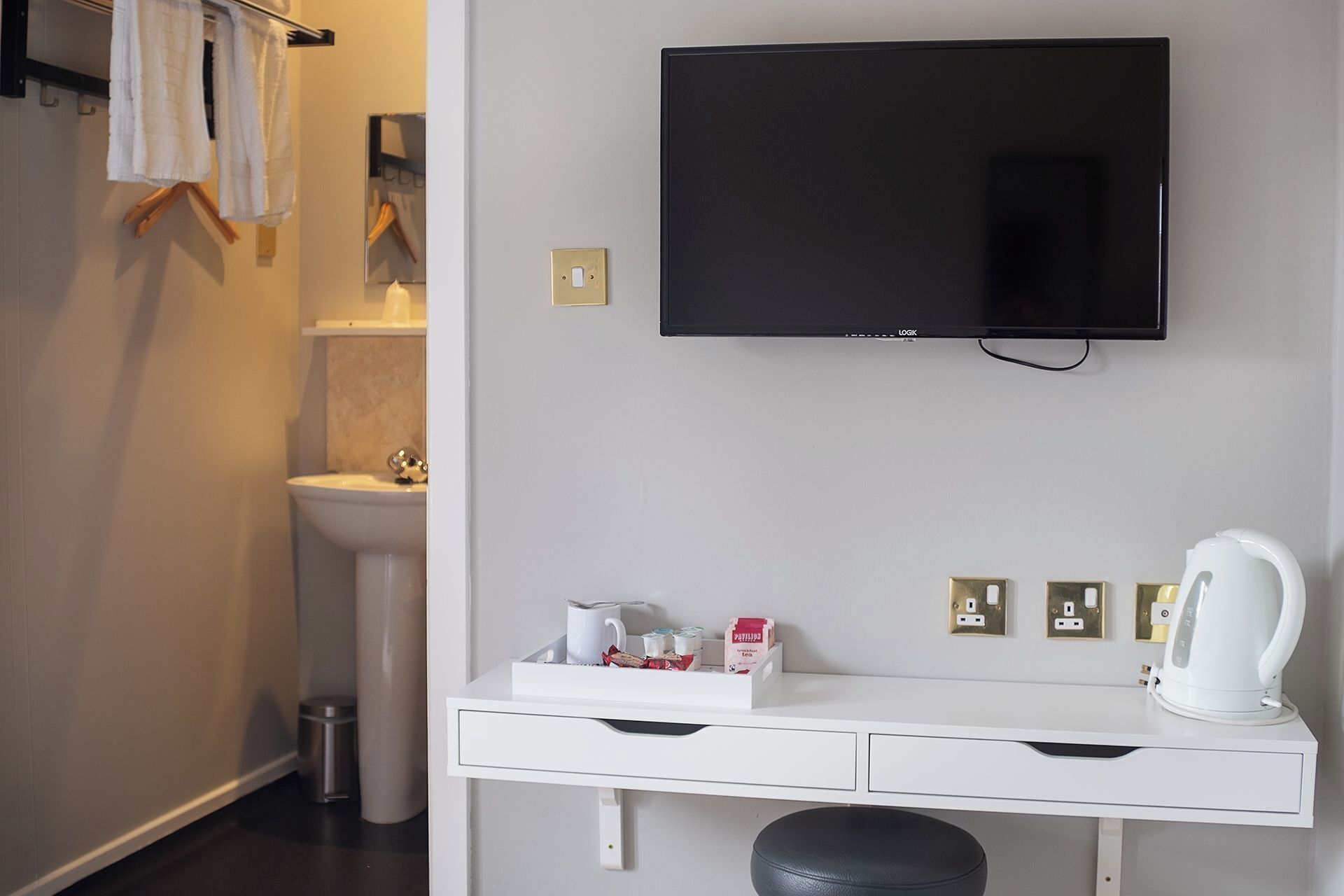A modern bathroom with a mounted TV, a white vanity with drawers, a toilet, and a sink.