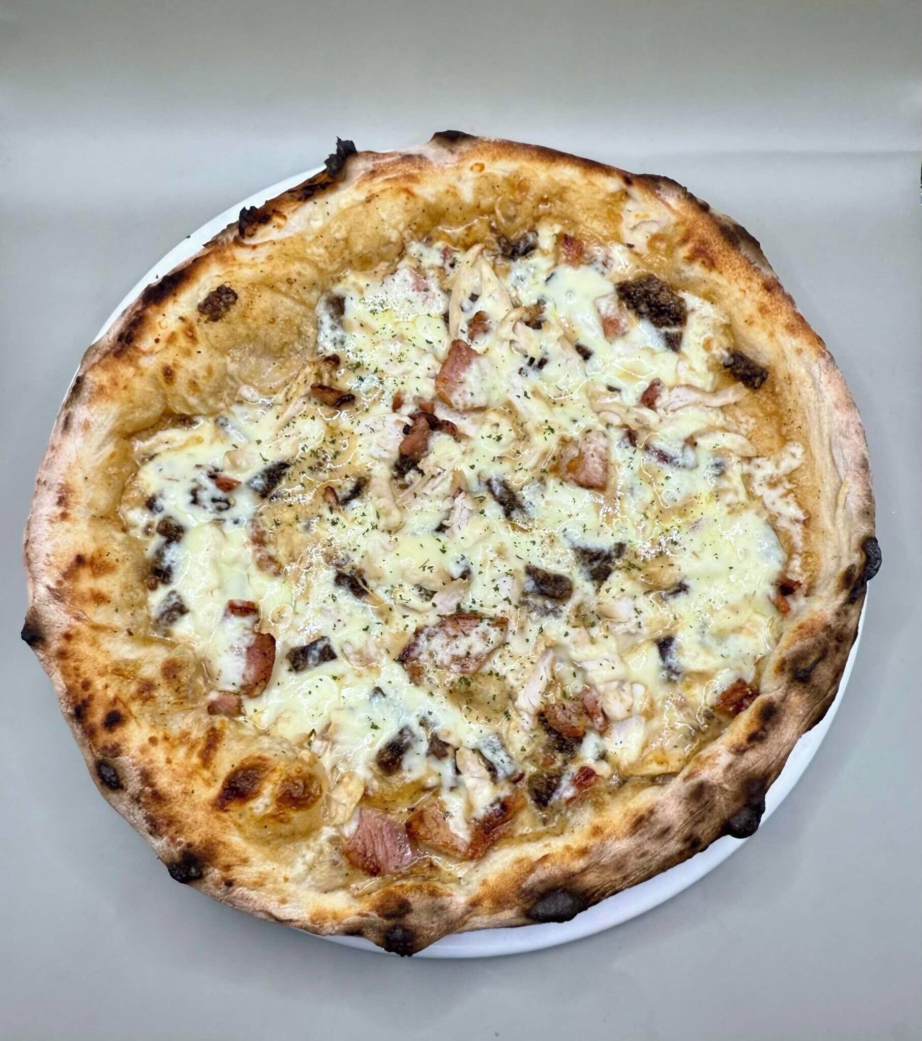 Pizza de masa gruesa cubierta de queso, champiñones y tocino, servida en un plato blanco.