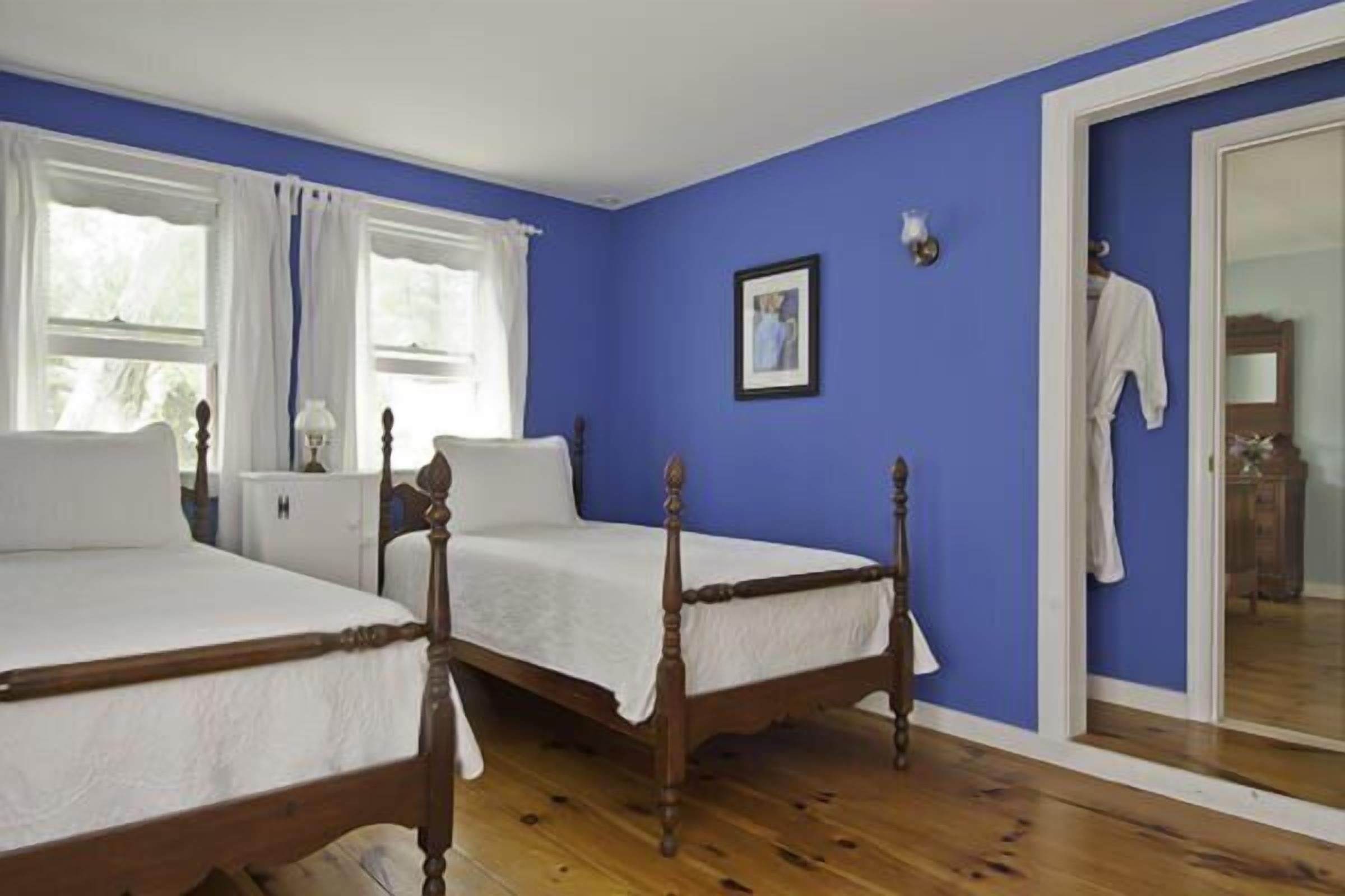 Ein Schlafzimmer mit zwei Holzbetten, weißer Bettwäsche, einer blauen Wand und einem Holzboden.