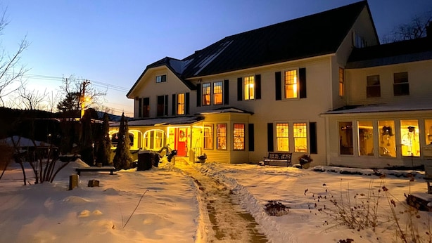 A two-story house with a snow-covered yard and a well-lit front porch. - Golden Stage Inn B&B (Cavendish)