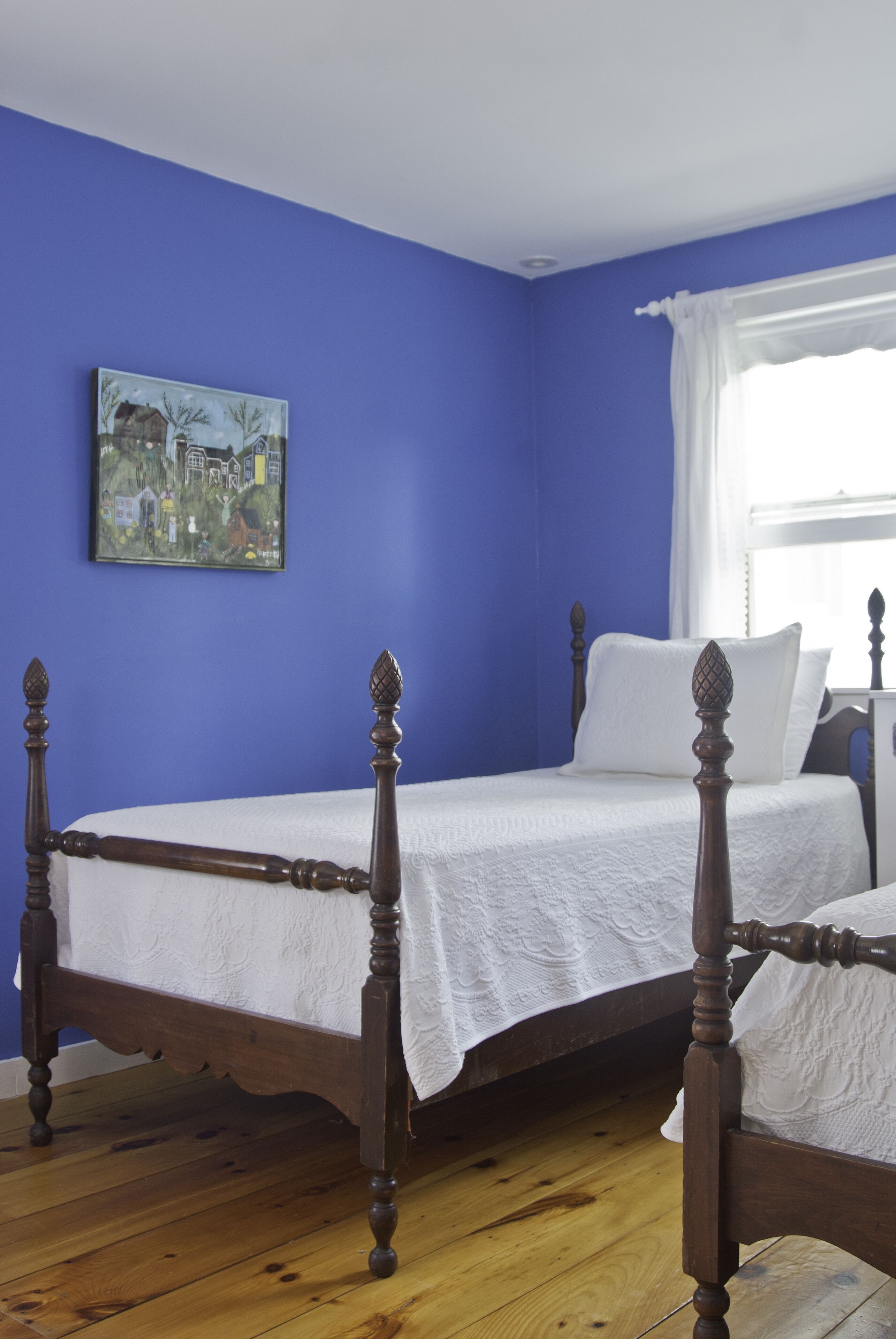 Una stanza con un letto, un quadro appeso al muro e una finestra con tende.