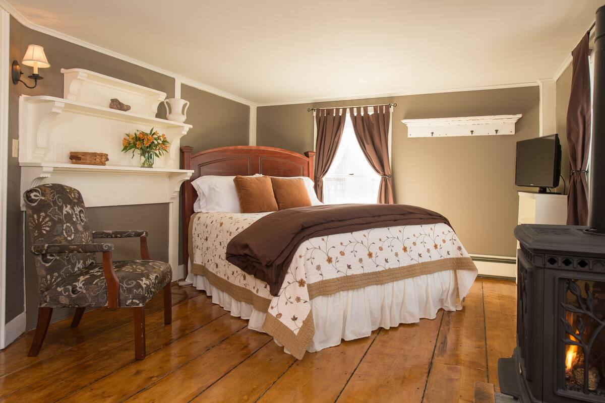 Ein Schlafzimmer mit einem hölzernen Bett, einem Sessel, einem Regal mit Dekoration und einem Kamin sowie einem Fernseher.