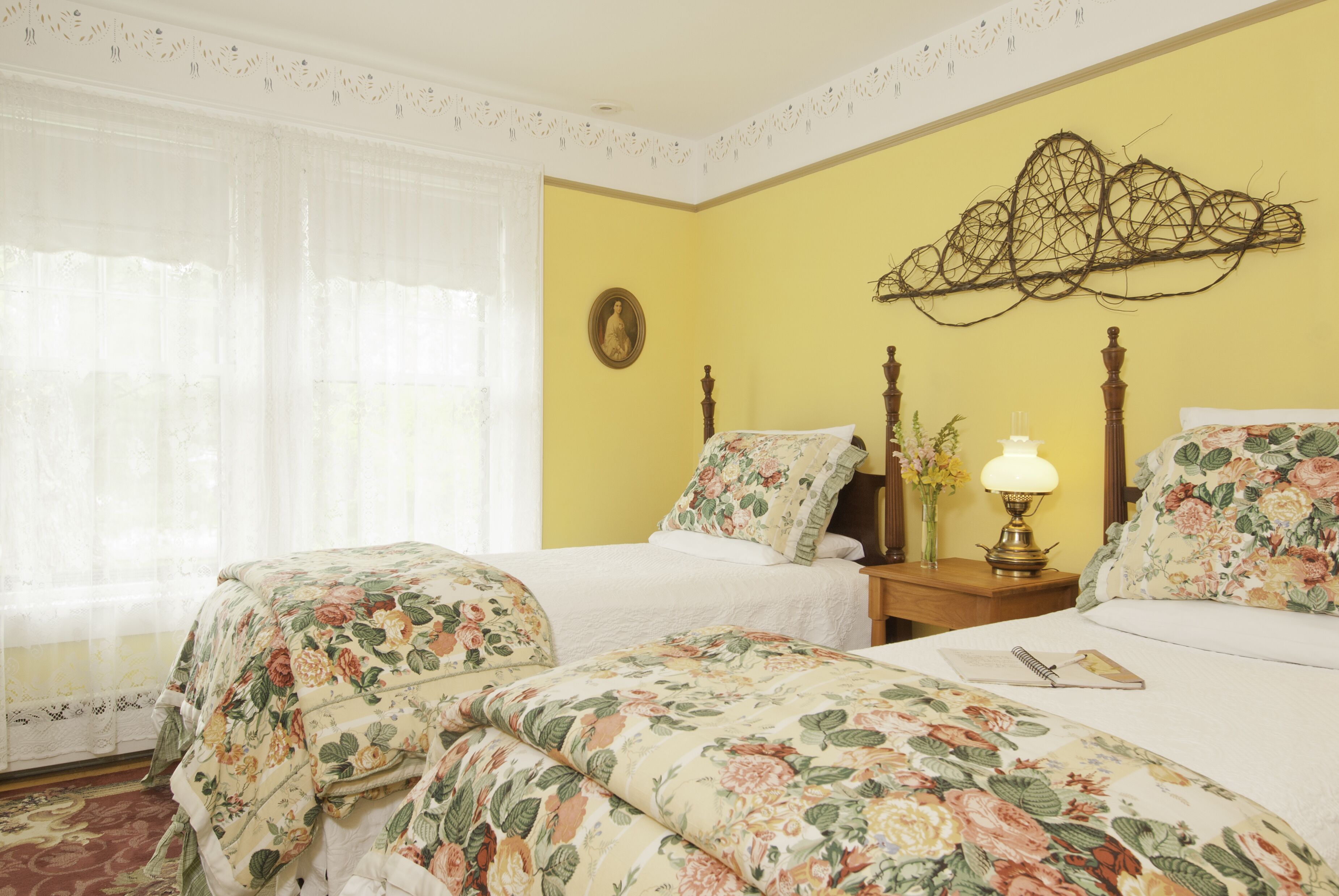 Habitación de hotel con dos camas, ropa de cama floral, una mesita de noche con lámpara y un adorno en la pared.