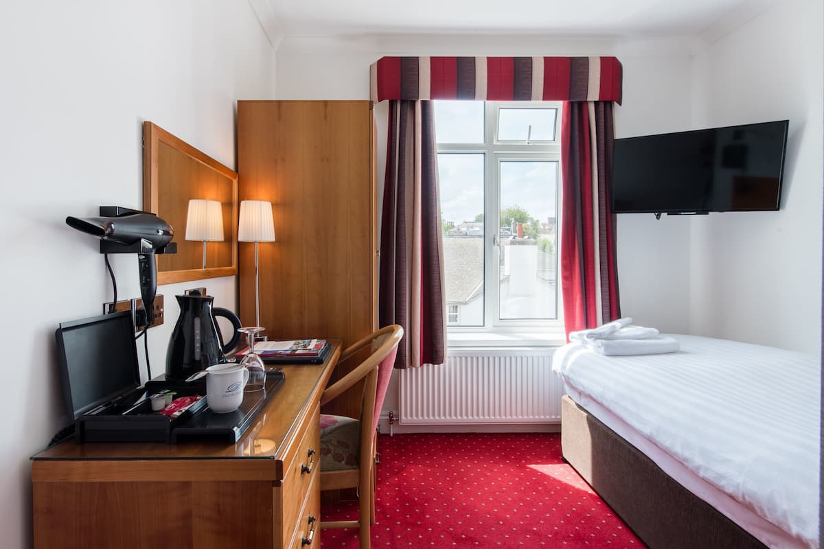 A hotel room with a bed, a desk with a computer, a coffee maker, and a TV.