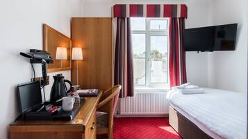 A hotel room with a bed, a desk with a computer, a coffee maker, and a TV.
