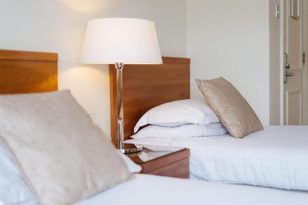 A hotel room with a wooden headboard, a bedside lamp, and a bed with white bedding and a beige pillow.