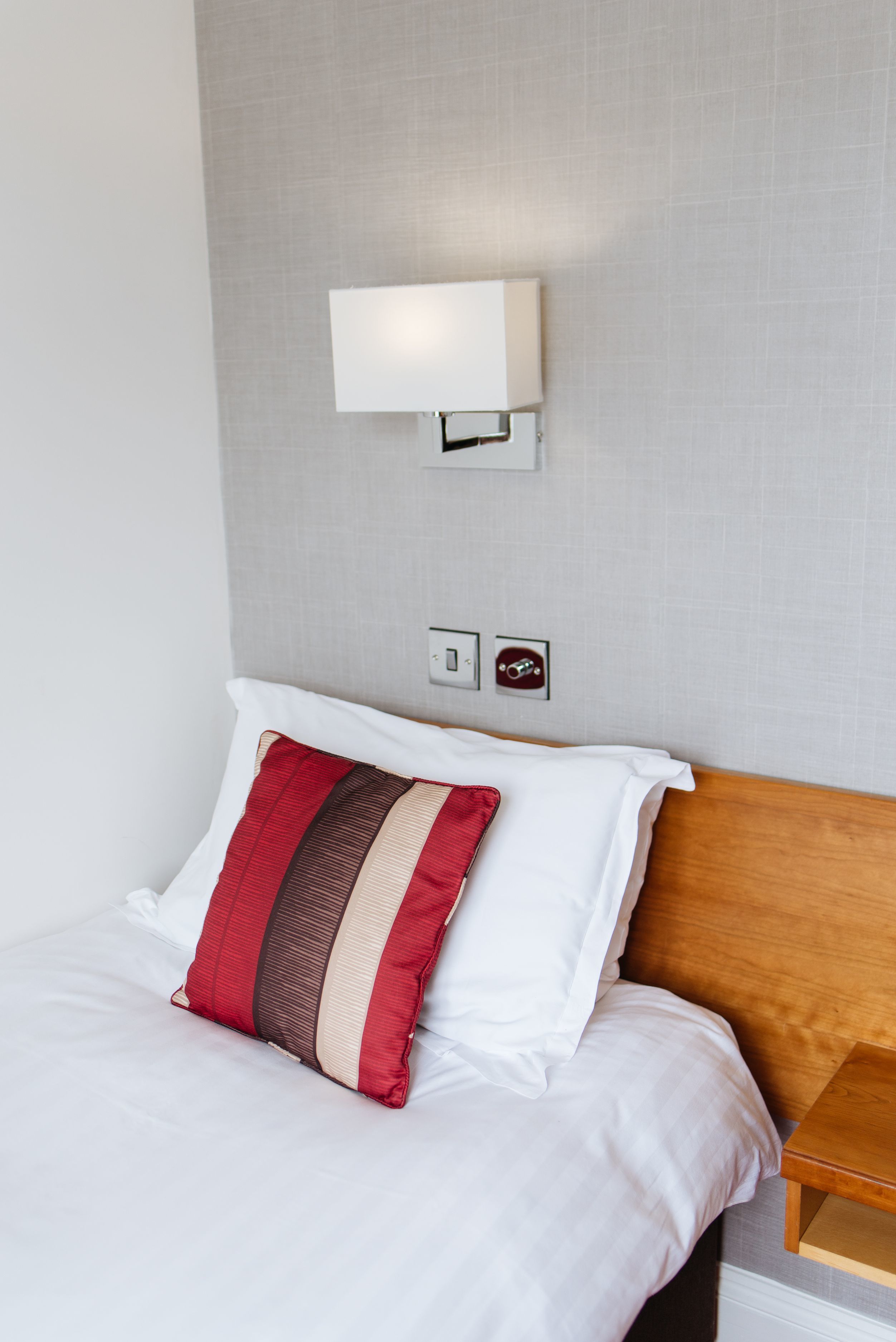 Una cama bien hecha con ropa de cama blanca y una almohada a rayas beige y roja.