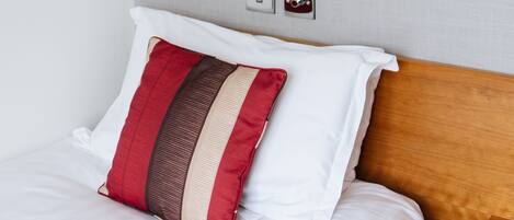 Una cama bien hecha con ropa de cama blanca y una almohada a rayas beige y roja.