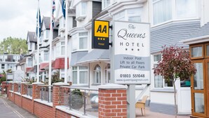 Señal de hotel con el nombre "The Queens Hotel" y los servicios indicados, incluyendo piscina cubierta, ascensor a todos los pisos y estacionamiento privado.
