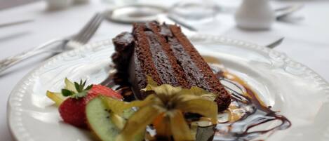 A dessert plate with a chocolate cake, strawberries, kiwi, and a decorative leaf.