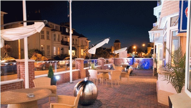 Un patio al aire libre con mobiliario de mimbre, una escultura metálica decorativa en el centro y piso de ladrillo.