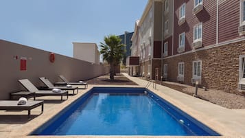 A swimming pool with lounge chairs and a palm tree, surrounded by multi-story buildings.