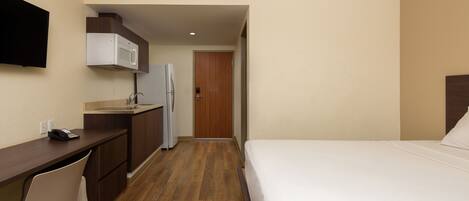 Habitación de hotel con cama, escritorio, microondas, refrigerador y puerta de madera.