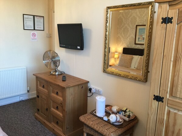 A hotel room with a wooden dresser, a mirror, a television, a radiator, and a small table with a tea set. - Balmoral (Skegness)