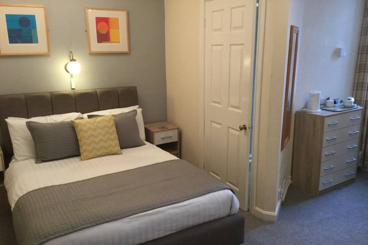 A neatly arranged bedroom with a large bed, bedside tables, a wardrobe, and framed artwork on the wall.
