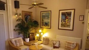 A cozy living room with a sofa, two armchairs, a small table, and a ceiling fan. There are two framed posters on the wall. - Balmoral (Skegness)