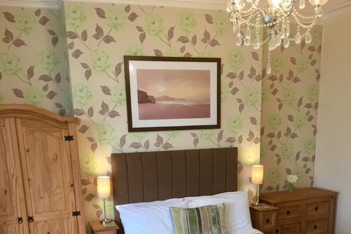 A bedroom with a bed, wooden wardrobe, nightstands, and a chandelier.