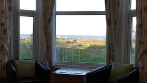 A room with a bed, two armchairs, a small wooden table, and a large window with curtains. - Balmoral (Skegness)
