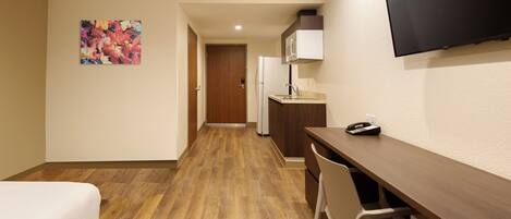 Habitación de hotel con cama, escritorio, silla, televisor, microondas y refrigerador.
