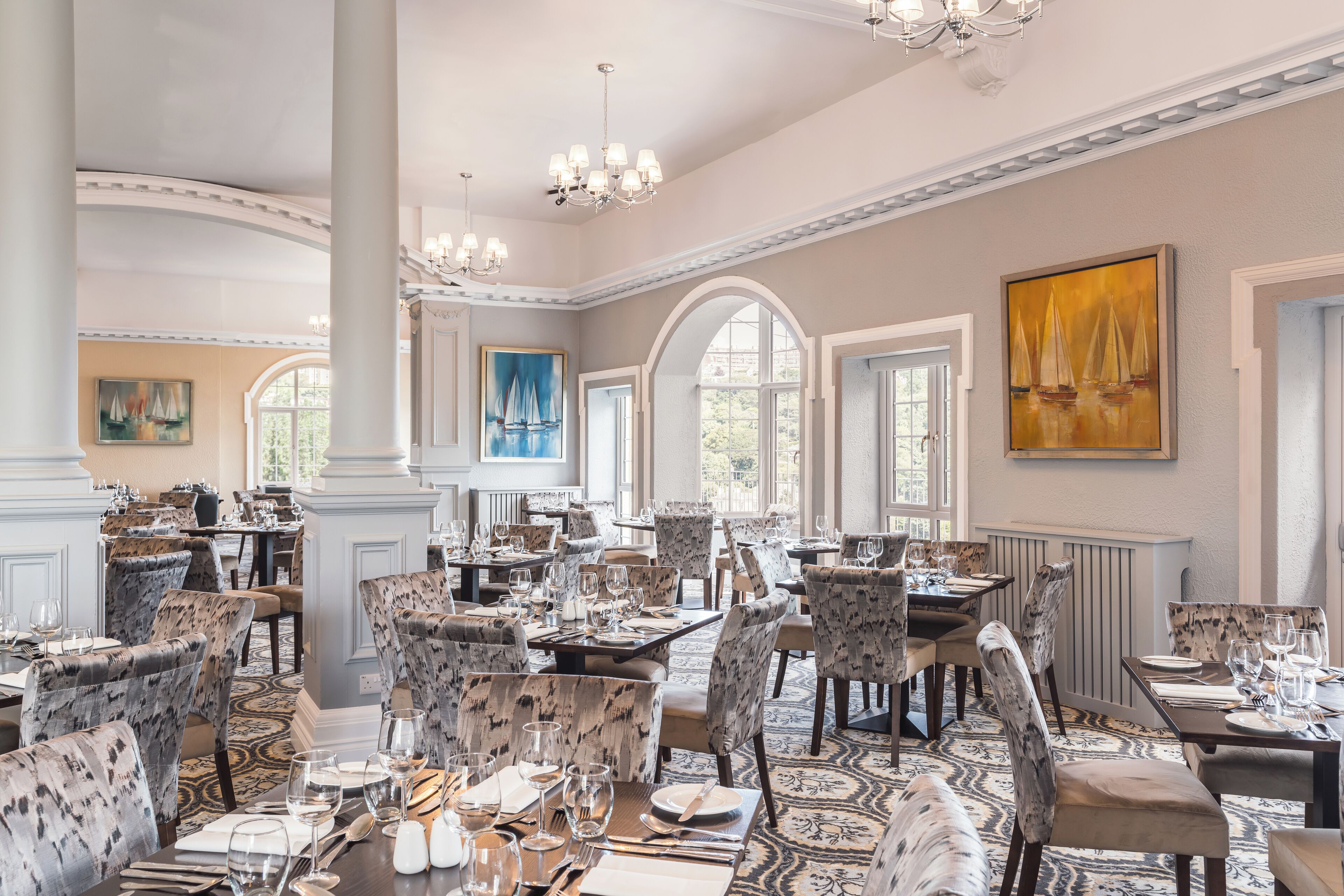 A spacious dining area with high ceilings, chandeliers, and a patterned carpet.