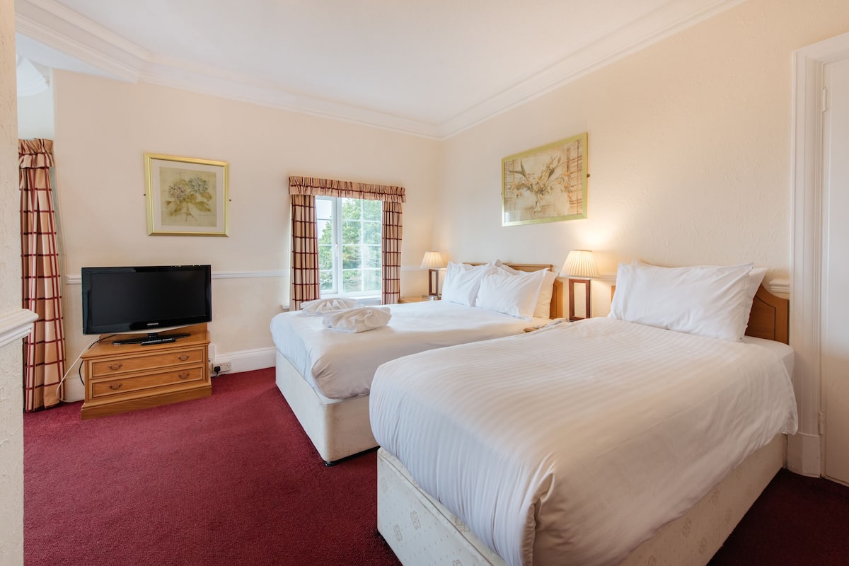 A hotel room with two beds, a TV, and artwork on the walls.