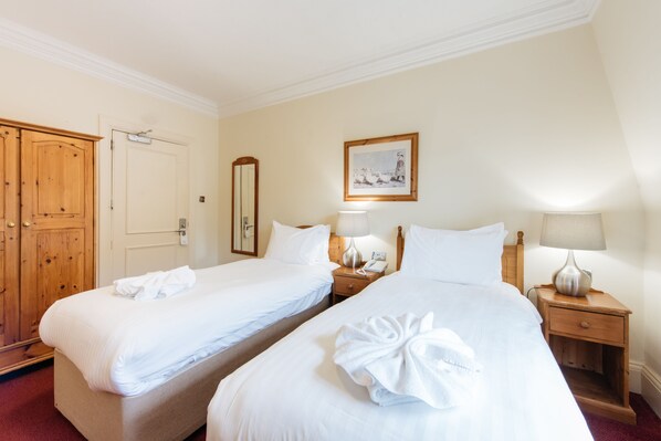 A hotel room with two beds, a wooden wardrobe, a mirror, a painting, and bedside lamps. - The Headland Hotel & Spa (Torquay)