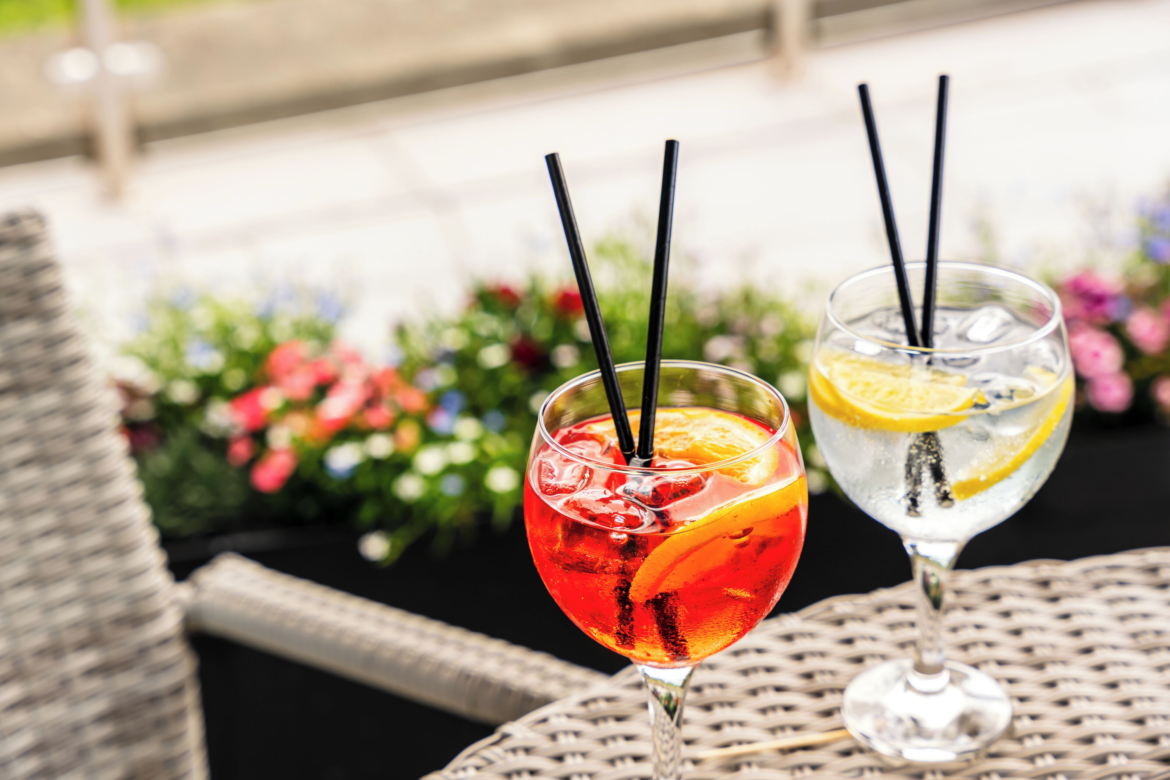 Two drinks on a wicker table with a garden background.