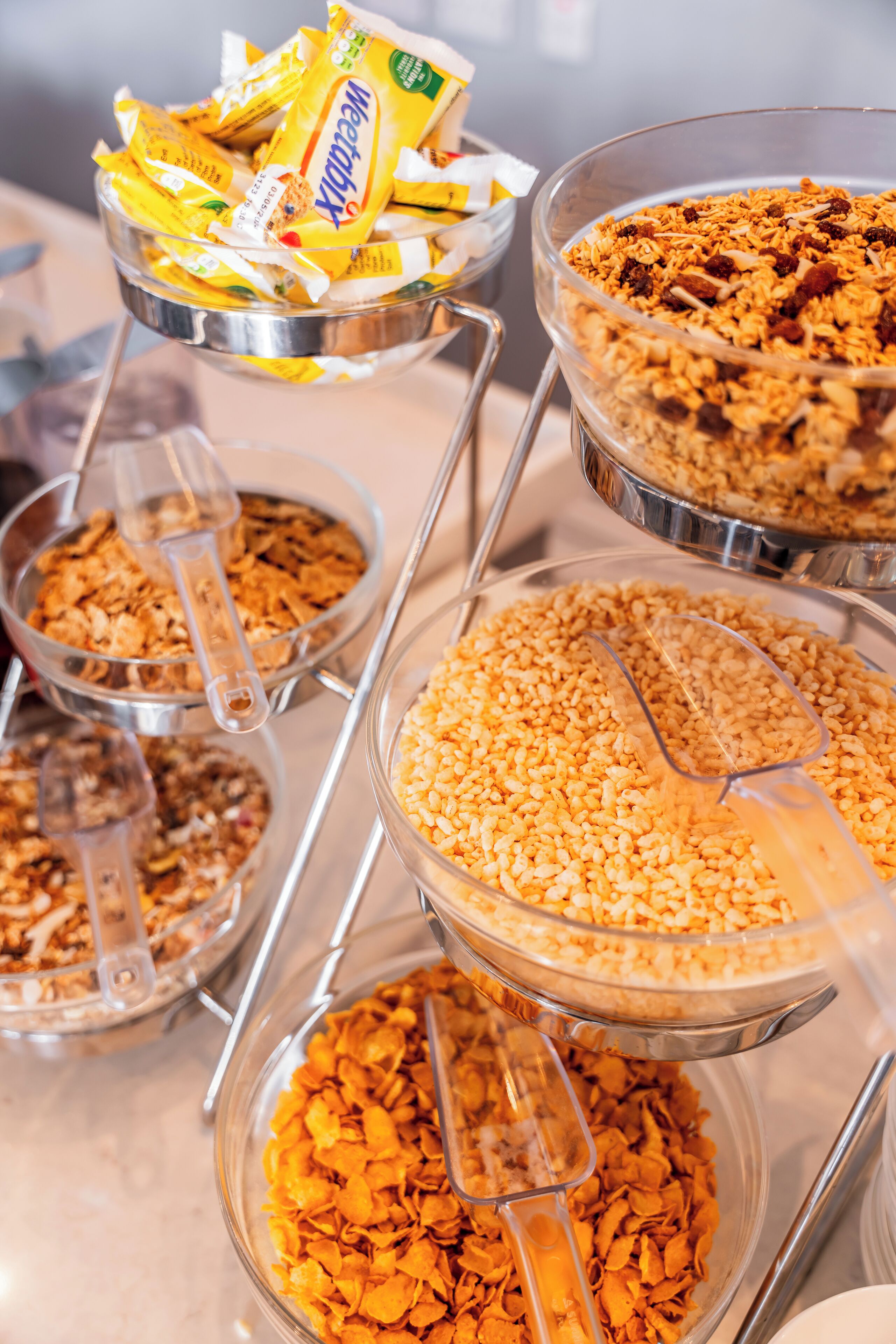 A buffet with various food items in clear bowls, including cereal and granola.