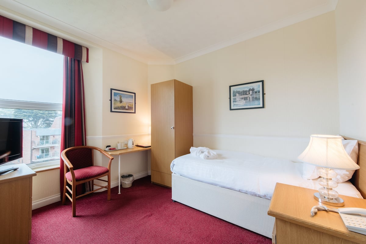 A hotel room with a bed, a desk, a chair, a TV, and a window with curtains.