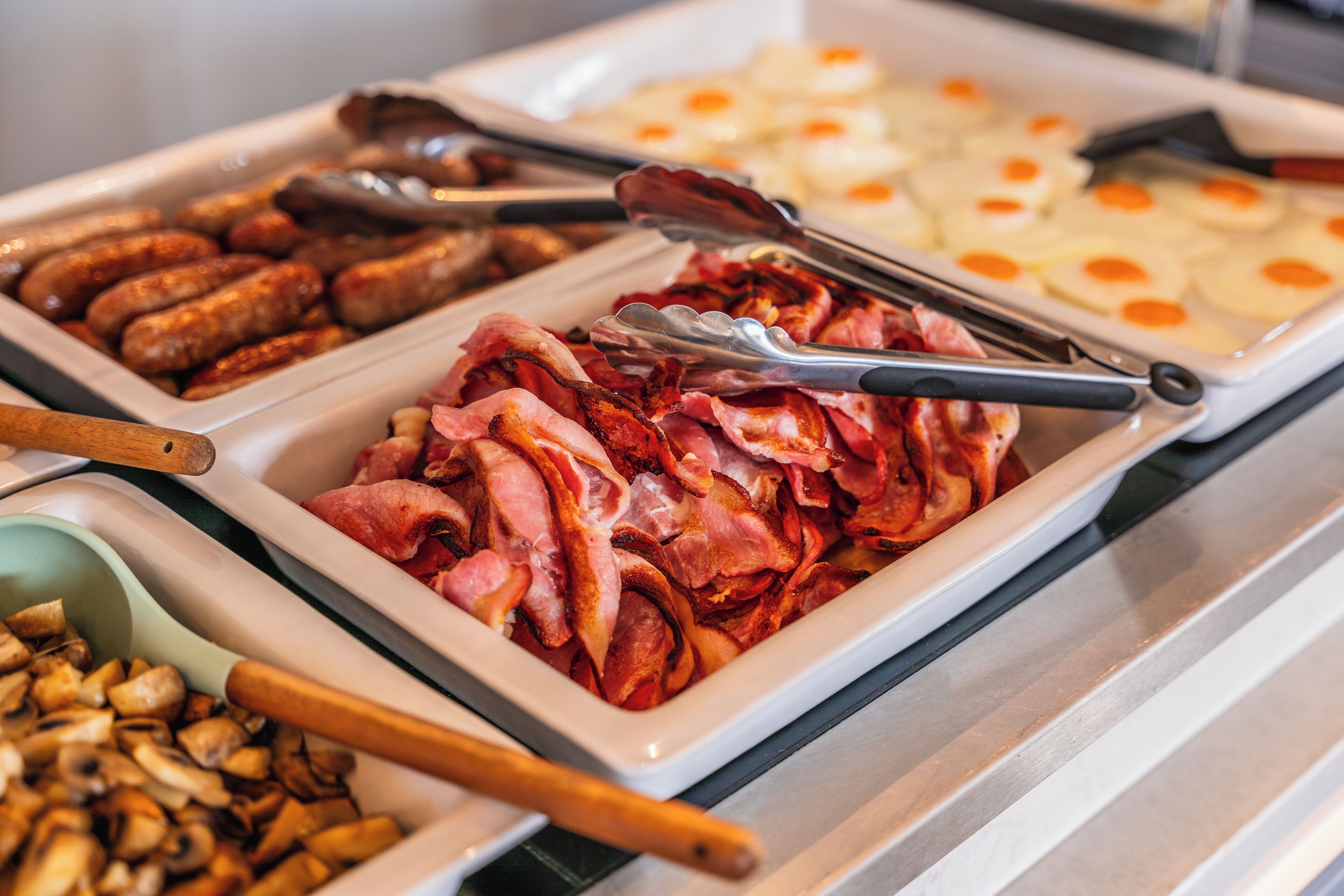 En buffé med ett varierat utbud av mat, inklusive korv, bacon, svamp och stekta ägg.