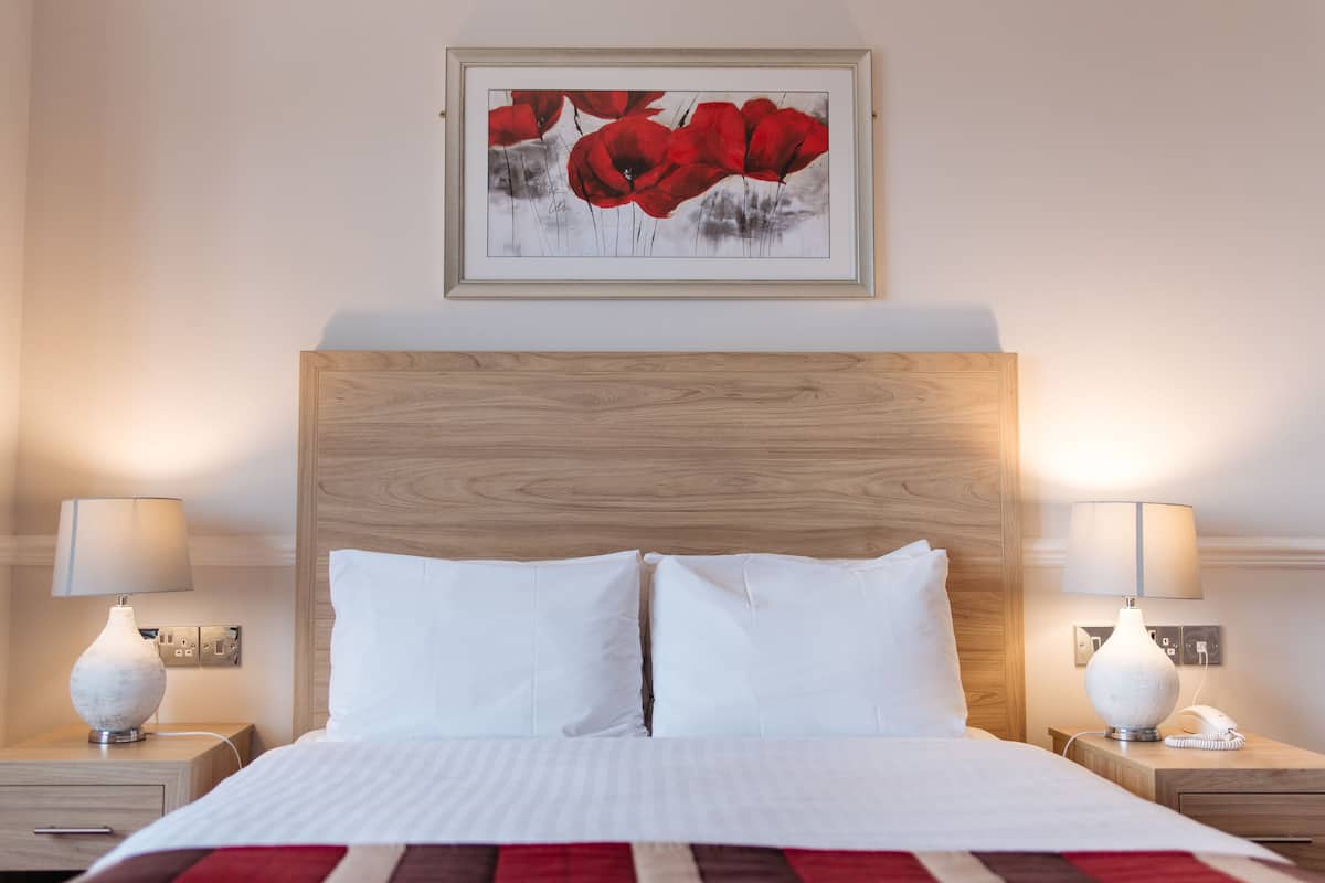 A neatly made bed with white linens, two bedside tables with lamps, and a framed artwork above the bed.