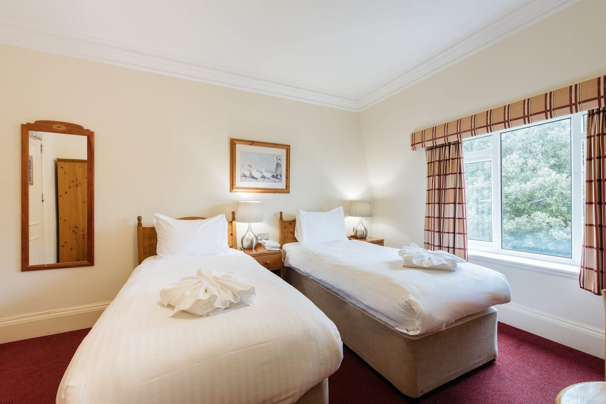 A hotel room with two beds, a large mirror, a framed picture, and a window with curtains.